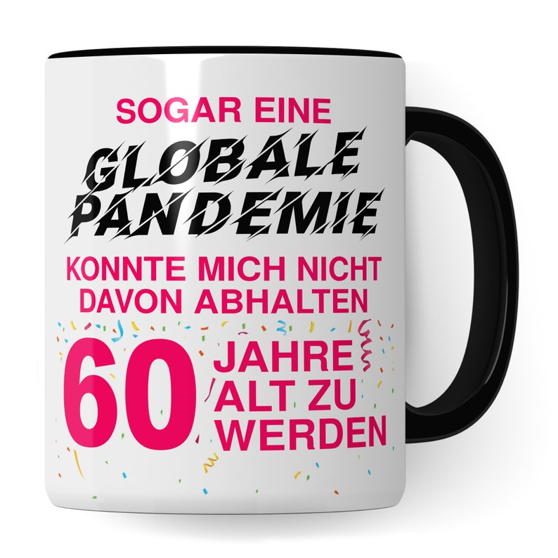 May include: White ceramic mug with a black handle. The mug has a pink and black design with the text "SOGAR EINE GLOBALE PANDEMIE KONNTE MICH NICHT DAVON ABHALTEN 60 JAHRE ALT ZU WERDEN".