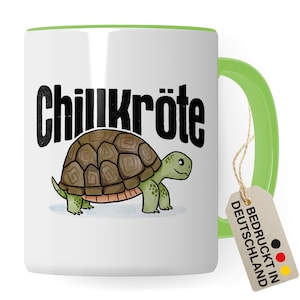 Può includere: Tazza in ceramica bianca con bordo e manico verdi. La tazza presenta una tartaruga dei cartoni animati con il testo "Chillkröte" in nero. La tazza ha un'etichetta marrone attaccata al manico che dice "Bedruckt in Deutschland" in nero con un cerchio rosso, giallo e nero.