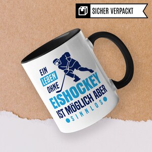 Pu&ograve; includere: Tazza in ceramica bianca con manico nero. La tazza presenta una grafica blu e nera di un giocatore di hockey con il testo "Ein Leben Ohne Eishockey Ist M&ouml;glich Aber Sinnlos".