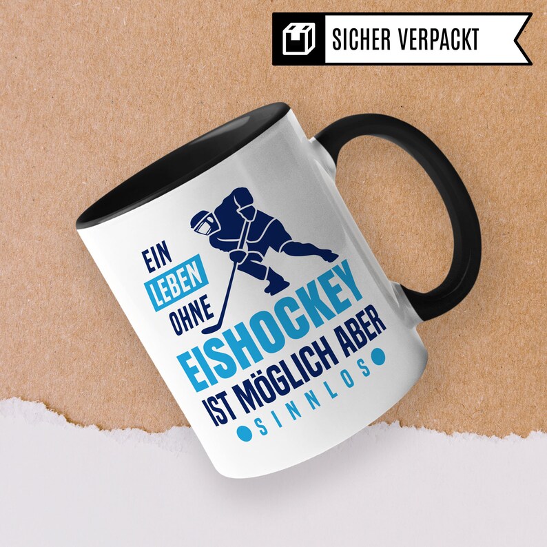 Pu&ograve; includere: Tazza in ceramica bianca con manico nero. La tazza presenta una grafica blu e nera di un giocatore di hockey con il testo "Ein Leben Ohne Eishockey Ist M&ouml;glich Aber Sinnlos".