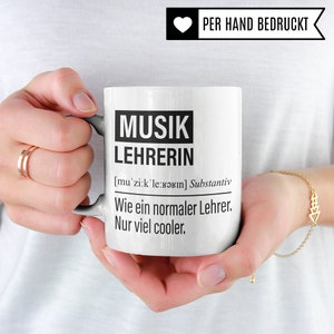 May include: White ceramic mug with black text that reads "MUSIK LEHRERIN [mu'zi:k'le:bərın] Substantiv Wie ein normaler Lehrer. Nur viel cooler."