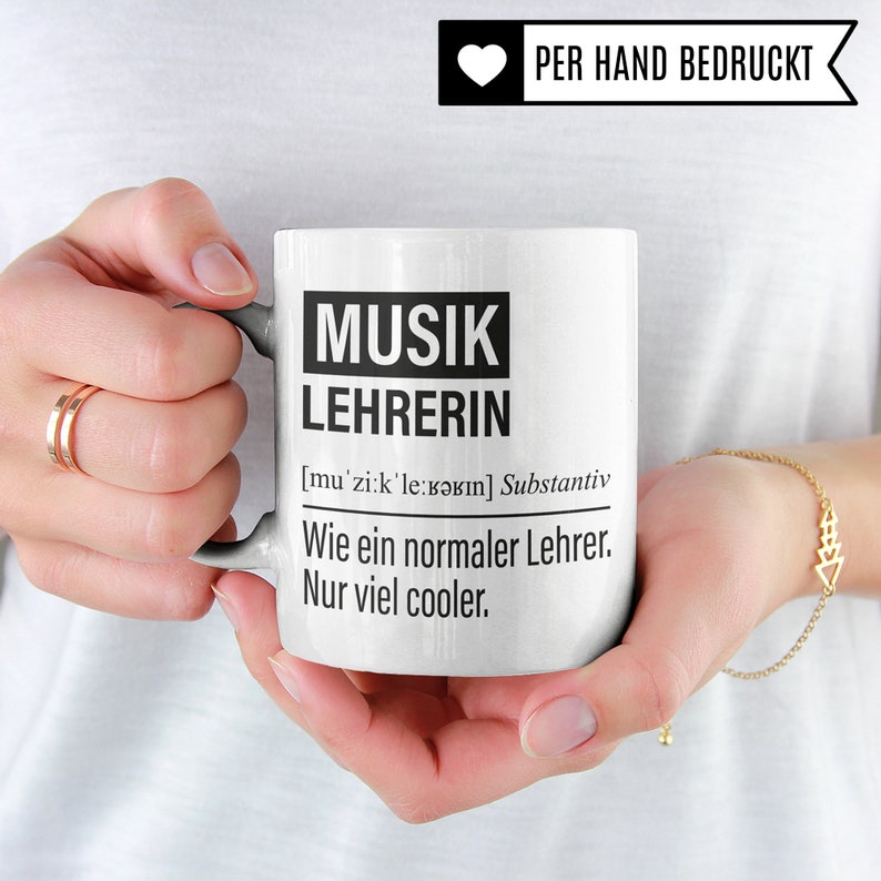 May include: White ceramic mug with black text that reads "MUSIK LEHRERIN [mu'zi:k'le:bərın] Substantiv Wie ein normaler Lehrer. Nur viel cooler."
