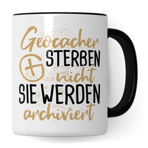 Könnte beinhalten: Weiße Keramiktasse mit schwarzem Rand und Henkel. Die Tasse hat ein schwarzes und goldenes Design mit dem Text "Geocacher sterben nicht sie werden archiviert".