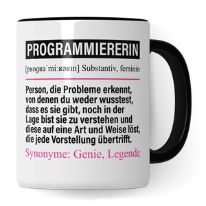 Pode incluir: Caneca de cerâmica branca com borda e alça pretas. A caneca apresenta um gráfico preto e rosa com o texto "PROGRAMMIERERIN" e uma definição em alemão. A definição inclui o texto "Person, die Probleme erkennt, von denen du weder wusstest, dass es sie gibt, noch in der Lage bist sie zu verstehen und diese auf eine Art und Weise löst, die jede Vorstellung übertrifft. Synonyme: Genie, Legende."
