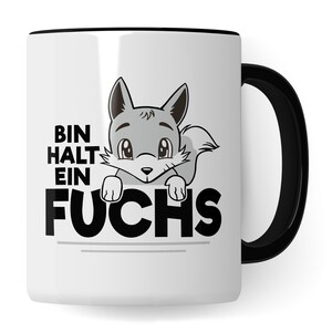 Könnte beinhalten: Weiße Keramiktasse mit schwarzem Rand und Henkel. Die Tasse zeigt einen Comic-Fuchs, der über das Wort "FUCHS" in schwarzer Schrift lugt. Der Text "BIN HALT EIN" befindet sich über dem Fuchs.