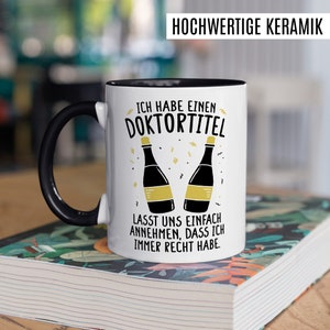 May include: White ceramic coffee mug with a black handle. The mug has a black rim and a graphic of two champagne bottles with the text "Ich habe einen Doktortitel. Lasst uns einfach annehmen, dass ich immer Recht habe."