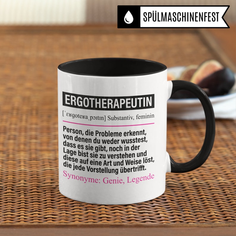 May include: White ceramic mug with a black rim and handle. The mug features a black and pink graphic with the text "ERGOTHERAPEUTIN" and a definition of the word in German. The text reads: "[ɛʁɡoːtɛʁaˈpɔɪ̯tɪn] Substantiv, feminin Person, die Probleme erkennt, von denen du weder wusstest, dass es sie gibt, noch in der Lage bist sie zu verstehen und diese auf eine Art und Weise l&ouml;st, die jede Vorstellung &uuml;bertrifft. Synonyme: Genie, Legende"