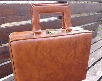 May include: A brown leather briefcase with a brass lock and handle. The briefcase is sitting on a wooden surface.