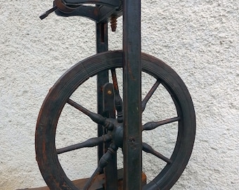 May include: A vintage wooden spinning wheel with a large dark brown wheel and a black wooden frame. The wheel has eight spokes and is mounted on a wooden stand.