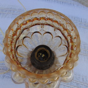 May include: A clear glass lampshade with a gold-toned finish. The lampshade has a scalloped edge and a textured design. The inside of the lampshade is visible, showing a light bulb socket.