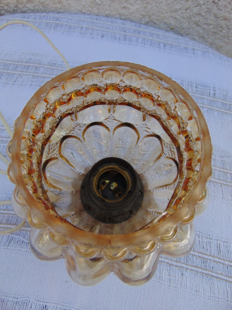May include: A clear glass lampshade with a gold-toned finish. The lampshade has a scalloped edge and a textured design. The inside of the lampshade is visible, showing a light bulb socket.