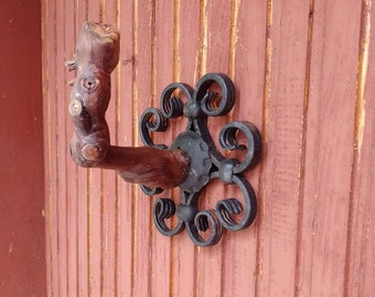 May include: A rustic wooden hook with a decorative black metal scroll design. The hook is mounted on a red wooden wall.