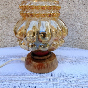May include: A vintage table lamp with a gold iridescent glass shade featuring a textured bubble design. The shade sits on a wooden base with a red accent.