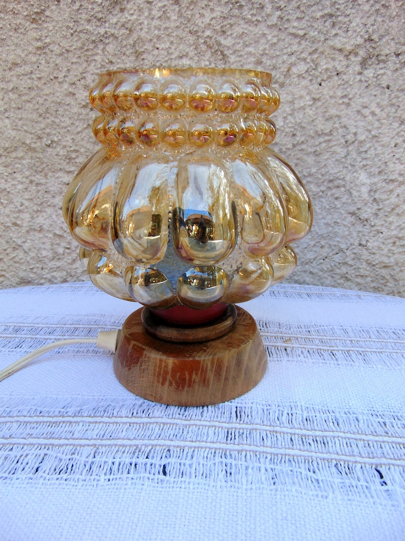 May include: A vintage table lamp with a gold iridescent glass shade featuring a textured bubble design. The shade sits on a wooden base with a red accent.