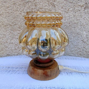 May include: A vintage table lamp with a gold iridescent glass shade featuring a textured bubble design. The lamp has a wooden base.