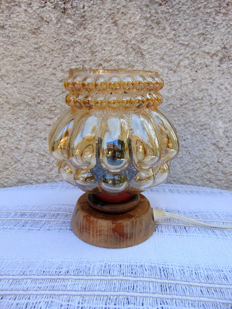 May include: A vintage table lamp with a gold iridescent glass shade featuring a textured bubble design. The lamp has a wooden base.