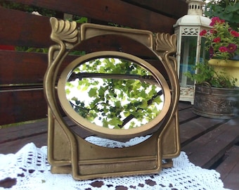 May include: A gold-toned, ornate, decorative mirror with a round, beveled glass. The mirror is sitting on a white crocheted doily.