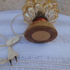 May include: A gold glass lamp shaped like a pine cone with a wooden base. The lamp has a cord and plug.