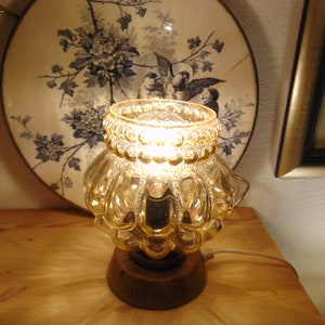 May include: A gold glass table lamp with a textured, bulbous shade and a wooden base. The lamp is lit and casting a warm glow.