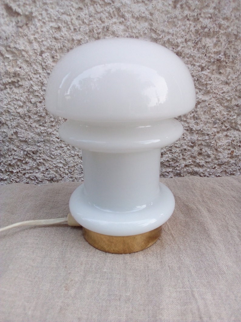 May include: A white glass table lamp with a mushroom-shaped shade and a gold base.