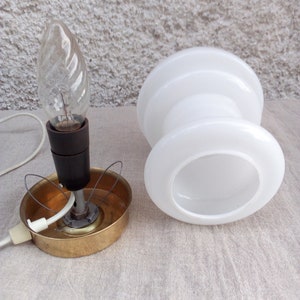 May include: A white glass lampshade with a brass base and a clear light bulb. The lampshade is shaped like a cylinder with a wider top and bottom.