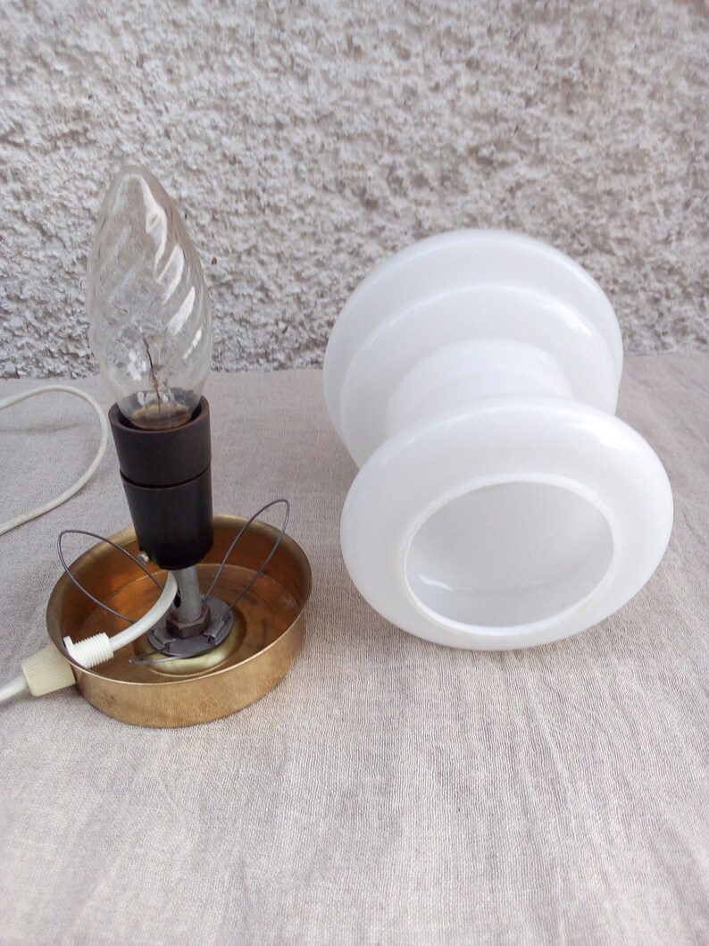 May include: A white glass lampshade with a brass base and a clear light bulb. The lampshade is shaped like a cylinder with a wider top and bottom.