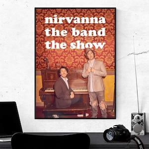 May include: A framed poster with the text "nirvanna the band the show" in white letters. The poster features two men in front of a piano. The background has a red and gold floral pattern. A laptop, camera, and radio are in the foreground.