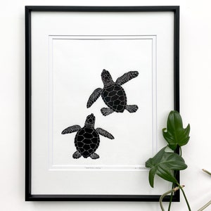 Puede incluir: L&aacute;mina art&iacute;stica en blanco y negro enmarcada, con dos tortugas marinas. Las tortugas tienen patrones de caparaz&oacute;n detallados y aletas extendidas. La impresi&oacute;n se titula "Hatchlings".