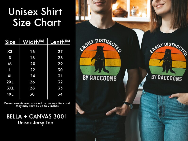 Op de afbeelding: Unisex zwart T-shirt met een retro-grafiek van een wasbeer en de tekst "Easily Distracted by Raccoons". Maattabel inbegrepen met metingen in inches.