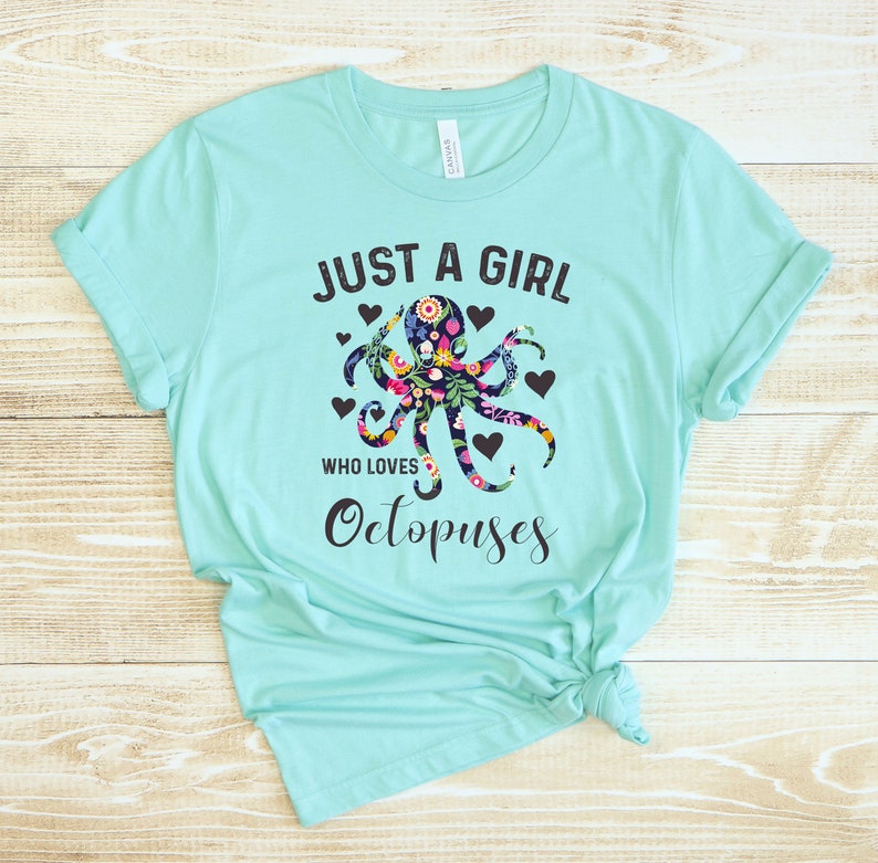 Puede incluir: Una camiseta turquesa con el texto "Just a girl who loves Octopuses" en negro. Un dise&ntilde;o de pulpo floral est&aacute; centrado en la camiseta.