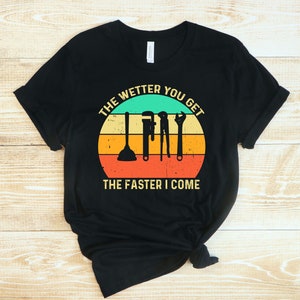 Puede incluir: Camiseta negra con un dise&ntilde;o retro que presenta herramientas de fontaner&iacute;a y el texto "THE WETTER YOU GET THE FASTER I COME" en un dise&ntilde;o circular con un fondo turquesa, amarillo, naranja y rojo.