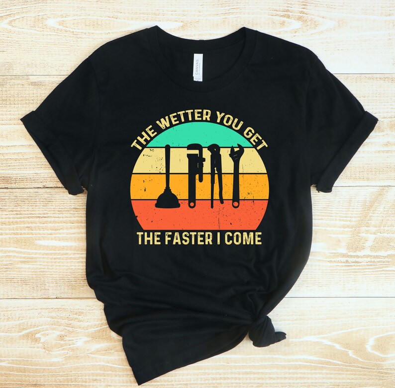 Puede incluir: Camiseta negra con un dise&ntilde;o retro que presenta herramientas de fontaner&iacute;a y el texto "THE WETTER YOU GET THE FASTER I COME" en un dise&ntilde;o circular con un fondo turquesa, amarillo, naranja y rojo.