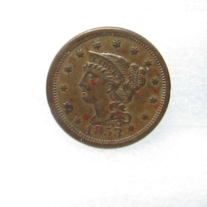 May include: A copper-colored coin from 1853, featuring a profile of a woman with a laurel wreath and stars around the edge. The coin has visible wear and tear, with some reddish discoloration.