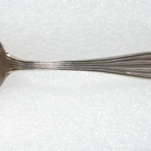 May include: A silver spoon with the words "Crystal Falls, Mich." engraved on the bowl. The handle features a detailed figure and decorative elements. The spoon is likely a souvenir or collectible item.