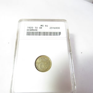 May include: A 1920 Denmark 10 OR coin in a clear protective case. The coin shows a crown above a stylized "C" and "X" design. The case has a label with the text "MS 64" and "DENMARK".