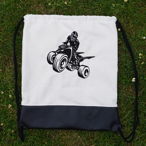 Könnte beinhalten: Weiße Kordeltasche mit einem schwarzen ATV- und Fahrer-Motiv. Die Tasche hat einen schwarzen Lederboden.