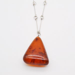 May include: A silver chain necklace with a large, triangular amber pendant. The amber is a deep orange color and has a natural, organic look.