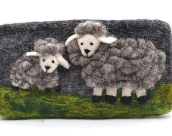 May include: A gray felt pouch with a zipper closure and a pom-pom pull. The pouch features a 3D design of two sheep on a green grassy area. The sheep are gray with white faces and ears.