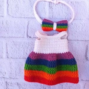 Pu&ograve; includere: Un vestito bianco all'uncinetto con strisce arcobaleno e una fascia per capelli abbinata con un fiocco arcobaleno.