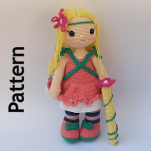 May include: A crocheted doll with blonde hair, a pink dress, and green shoes. The doll is holding a yellow and green wand with a pink flower on top. The doll is standing on a white background. The word "Pattern" is written vertically on the left side of the image.