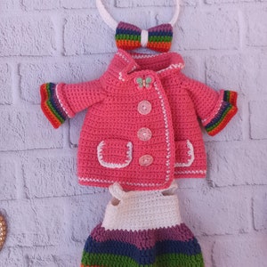 Pu&ograve; includere: Una giacca rosa all'uncinetto con bordi arcobaleno, un vestito bianco all'uncinetto con strisce arcobaleno e una fascia per capelli arcobaleno all'uncinetto con un fiocco.