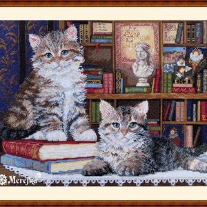 May include: Two tabby cats, one sitting on a stack of books and the other lying on a white doily, in front of a bookcase filled with books. The bookcase has a wooden frame and is decorated with a painting of a woman.