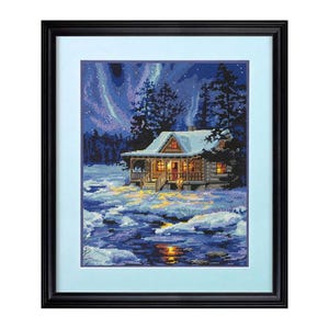 Könnte beinhalten: Ein gerahmtes Kreuzstich-Kunstwerk, das eine gemütliche Hütte zeigt, die in einem schneebedeckten Wald unter einem sternenklaren Himmel mit einer leuchtenden Aurora Borealis im Hintergrund liegt.