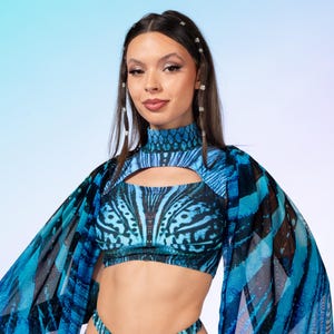 May include: A two-piece swimsuit set featuring a high-neck crop top with a chest cutout and high-cut bottoms with side cutouts. The fabric displays a vibrant blue and black butterfly wing pattern, complemented by sheer, flowing cape sleeves.