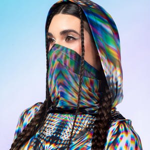 Könnte beinhalten: Ein kurzärmeliges Kapuzenoberteil mit einem lebendigen, mehrfarbigen psychedelischen Muster mit blauen, gelben und magentafarbenen Streifen. Das Kleidungsstück verfügt über eine integrierte Gesichtsbedeckung und einen runden Ausschnitt.