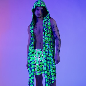 May include: A neon green and blue patterned outfit consisting of a hooded scarf, shorts, and a matching wrap. The design features a repeating smiley face motif. The person is wearing black boots and socks.