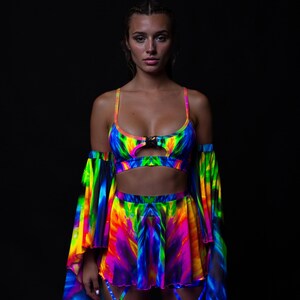 Könnte beinhalten: Ein leuchtendes, mehrfarbiges Outfit mit einem Crop-Top mit Schlüssellochdetail und einem passenden Rock. Das Ensemble umfasst lange, fließende Ärmel und ist mit einem Spektrum an leuchtenden Farben verziert, wodurch ein auffälliger visueller Effekt entsteht. Das Outfit ist für einen kühnen, auffälligen Look konzipiert.