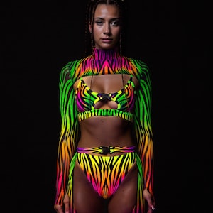 Puede incluir: Un conjunto de cebra con estampado de neón, que incluye un top corto, una parte inferior de cintura alta y un bolero de manga larga. El conjunto presenta vibrantes tonos de verde, amarillo, naranja, rosa y morado. El atuendo tiene un cuello alto y un detalle recortado.