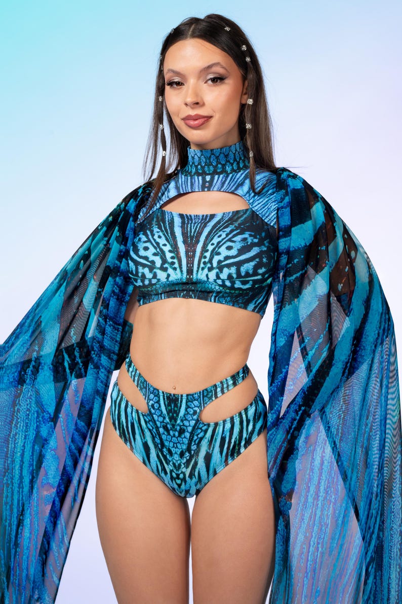 May include: A two-piece swimsuit set featuring a high-neck crop top with a chest cutout and high-cut bottoms with side cutouts. The fabric displays a vibrant blue and black butterfly wing pattern, complemented by sheer, flowing cape sleeves.