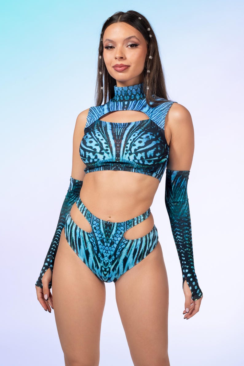 May include: A two-piece set featuring a high-neck sleeveless crop top with a chest cutout and high-waisted bottoms with side cutouts, both in a blue and black patterned print, accompanied by matching long arm sleeves with thumb holes.